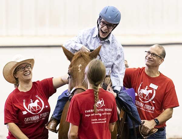 adults holding a horse while a teenager rides it